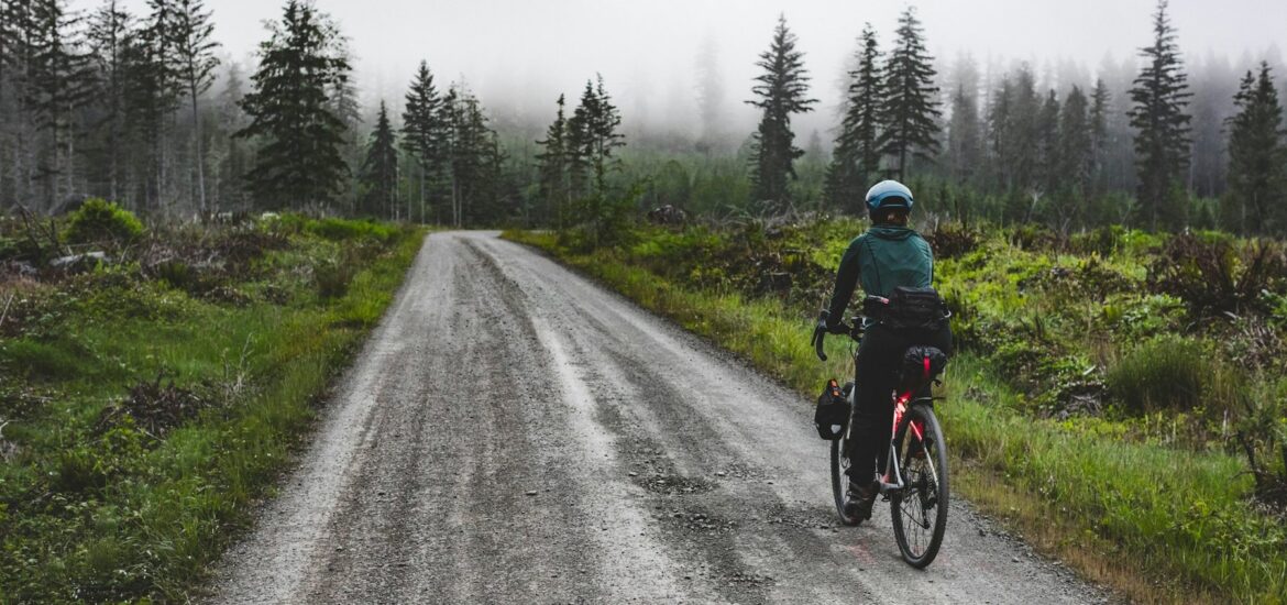 Cyclist riding a wet gravel road through a misty forest