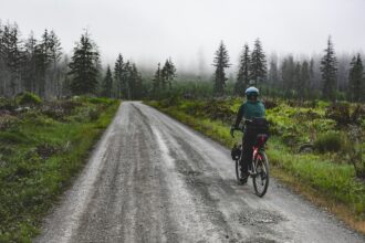 Cyclist riding a wet gravel road through a misty forest