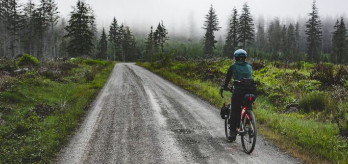 Cyclist riding a wet gravel road through a misty forest