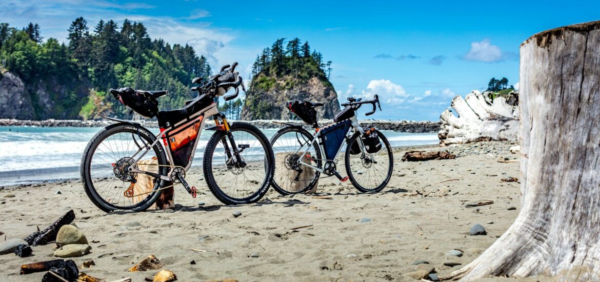 Two loaded touring bikes on a beach with sea stacks behind