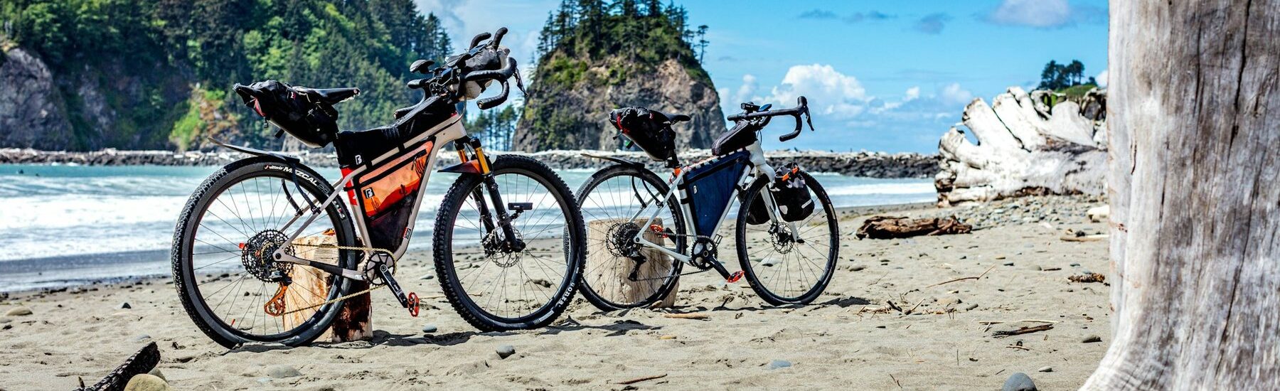Two loaded touring bikes on a beach with sea stacks behind