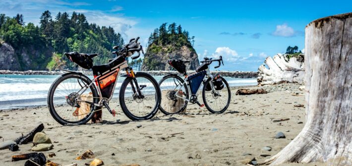 Two loaded touring bikes on a beach with sea stacks behind