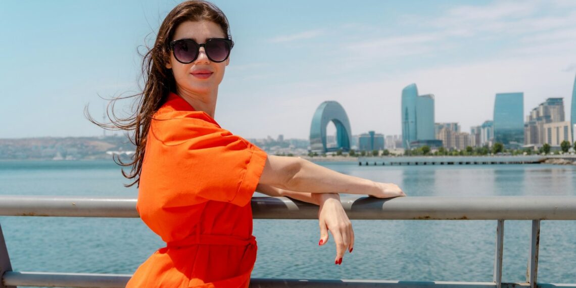 Woman in an orange dress and sunglasses leaning on the railing of the seaside boulevard
