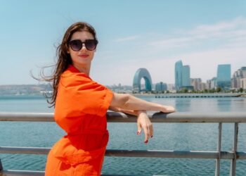 Woman in an orange dress and sunglasses leaning on the railing of the seaside boulevard