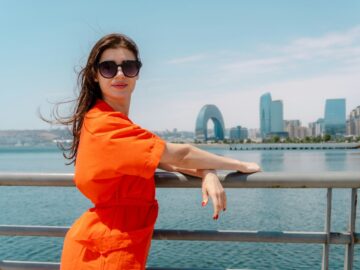Woman in an orange dress and sunglasses leaning on the railing of the seaside boulevard