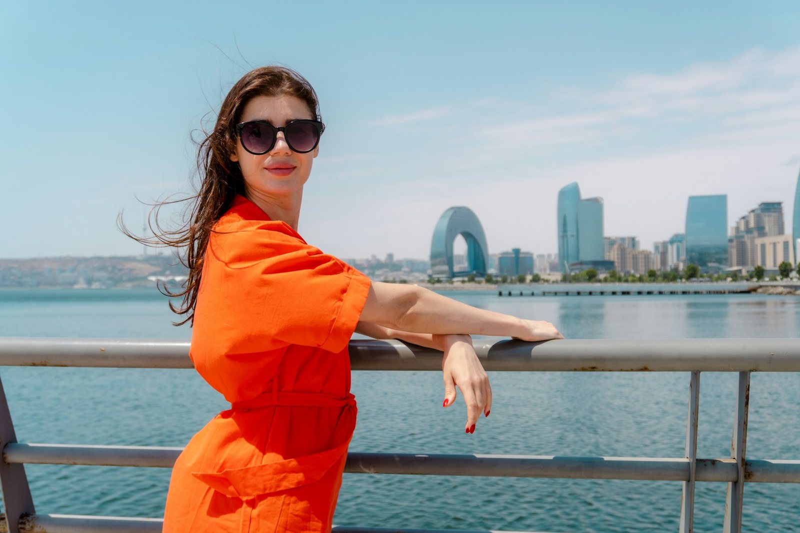 Woman in an orange dress and sunglasses leaning on the railing of the seaside boulevard