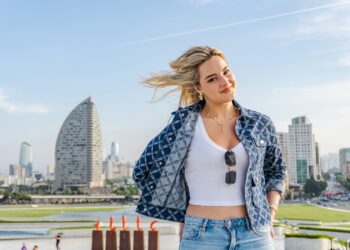 Smiling woman in a denim jacket with city towers behind her