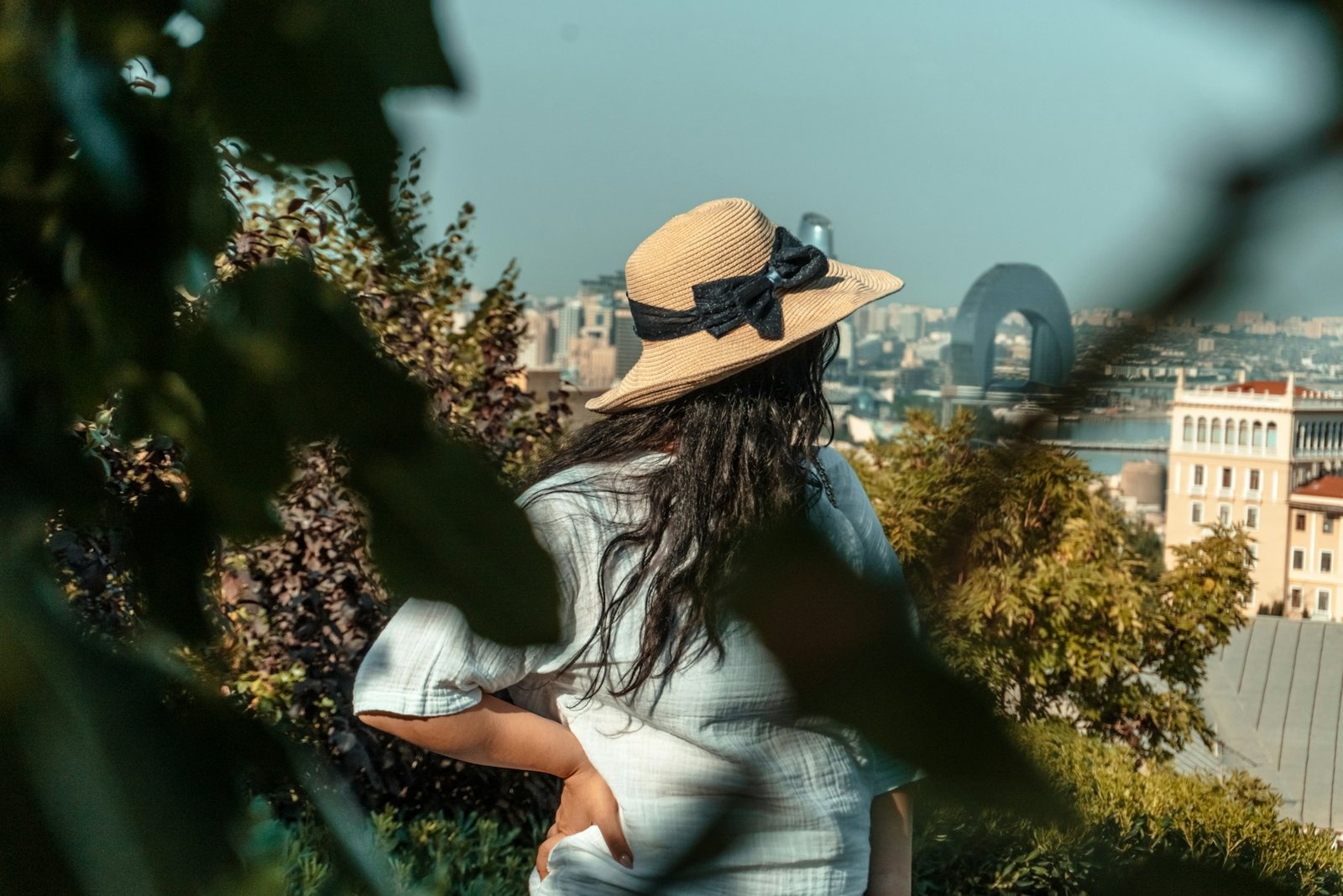 Woman in a straw hat looking over the city from a shady garden
