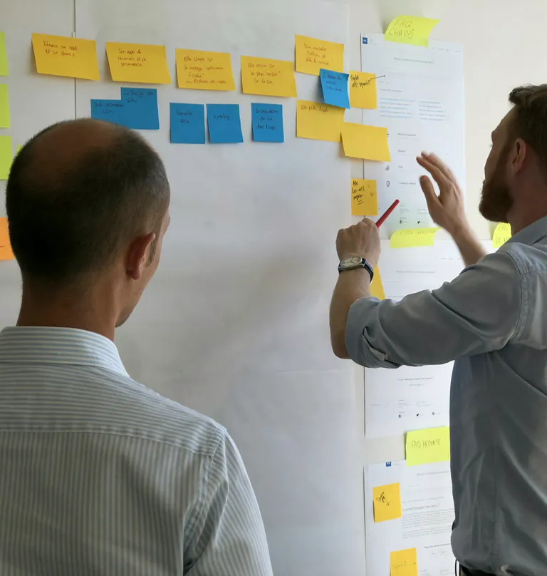 Two designers planning a project on a wall of sticky notes