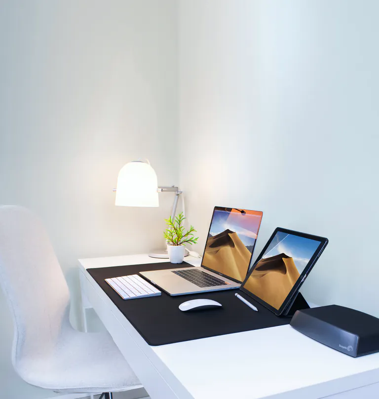 A tidy desk with a laptop and a tablet side by side under a lamp