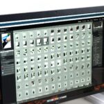 A designer at a large monitor showing a grid of hundreds of small image thumbnails