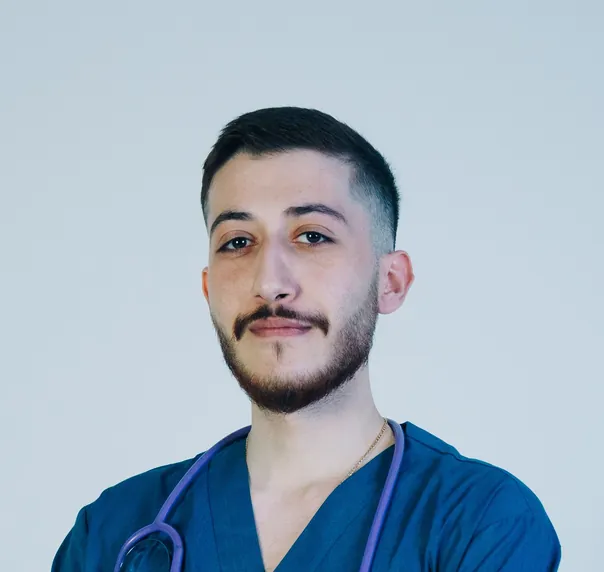 A bearded young man in royal blue scrubs with a stethoscope, arms folded