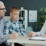 A grandfather and his grandson in a consultation with a doctor, who is pointing at her notes
