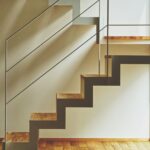 A folded white steel stair with oak treads climbing a sunlit white wall above an oak floor