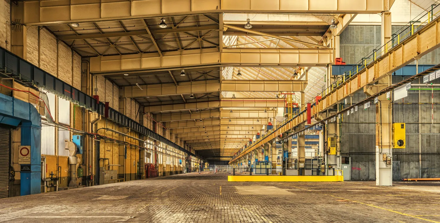 A long, sunlit industrial hall with steel roof trusses and a yellow gantry crane