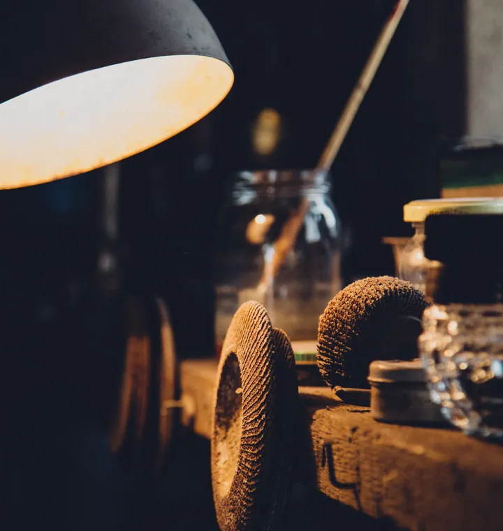 A workshop lamp lighting a bench grinder and glass jars on a dark workbench