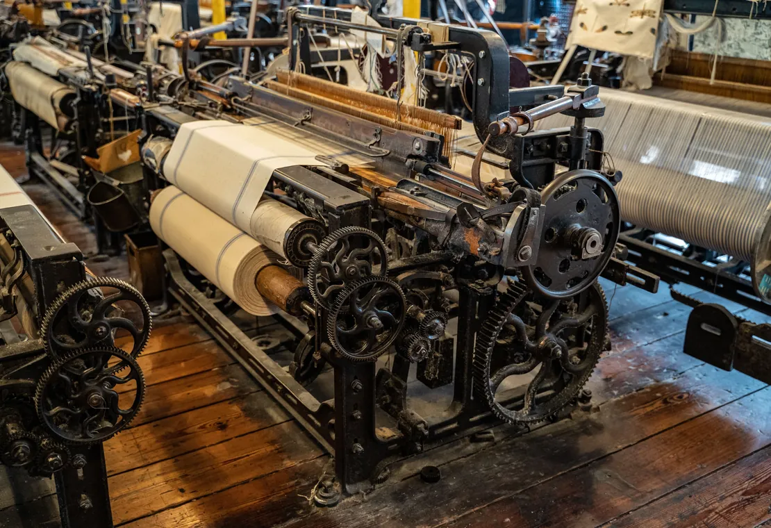 Rows of cast-iron looms with white cloth beams in a textile mill