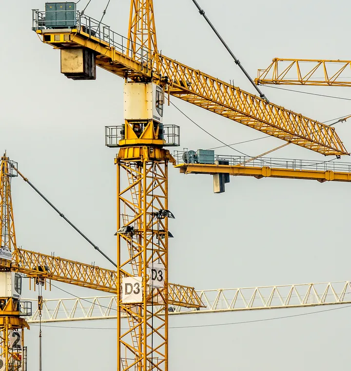 Two yellow tower cranes against a pale sky