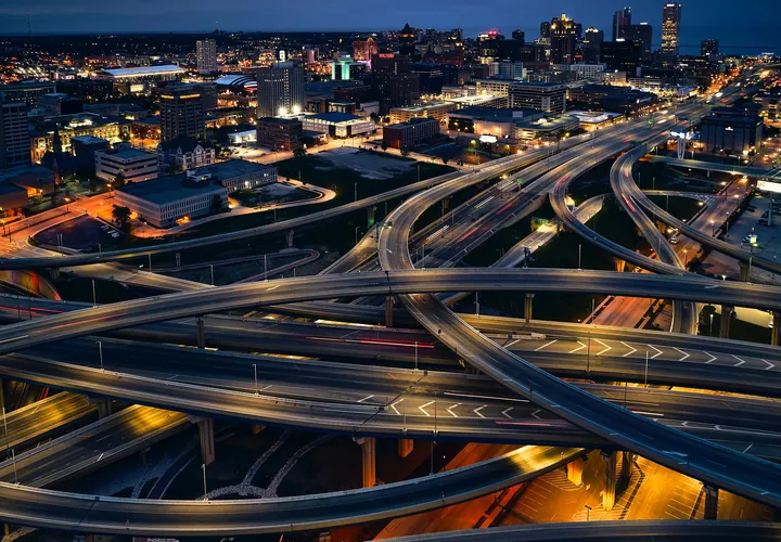 A multi-level highway interchange lit up at dusk, with a city behind it