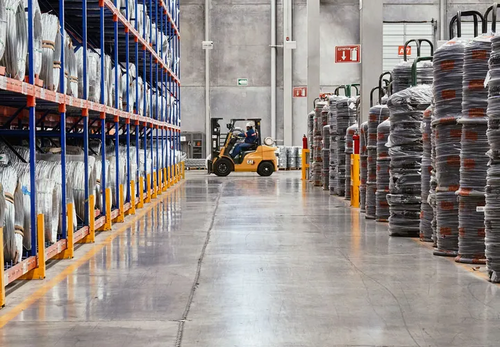 A long warehouse aisle between blue racking, a forklift at the far end