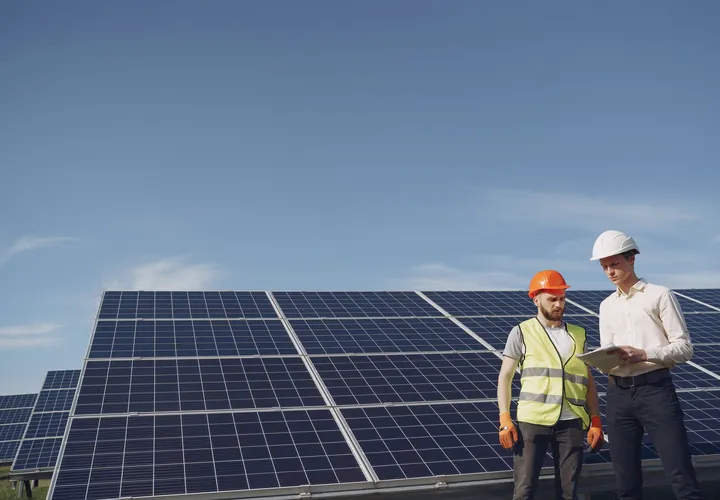 Two engineers in hard hats beside a field of solar panels under a blue sky