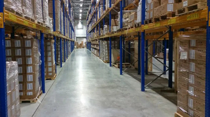 A long, bright warehouse aisle between blue and yellow pallet racking