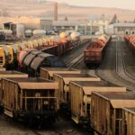 Rows of rust-brown hopper wagons and tank cars in a freight yard under a hazy golden sky