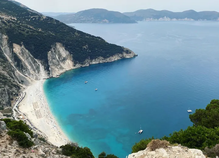 Myrtos beach on Kefalonia from the road above, a white crescent of pebbles between steep cliffs and deep blue water