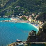 Monterosso al Mare from the hill above: a long curve of beach, the old town behind it and green terraced slopes running down to the sea