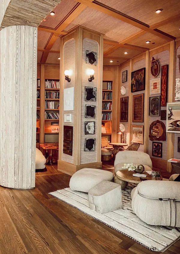 A hotel lounge with pale armchairs round a low table, bookshelves and framed pictures on timber walls