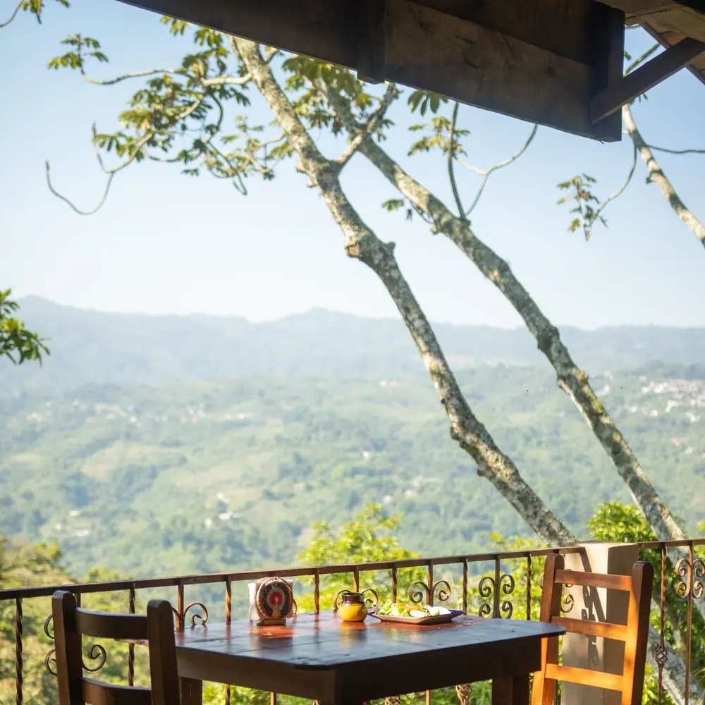 A table for two on a timber terrace under the trees, a green valley falling away below