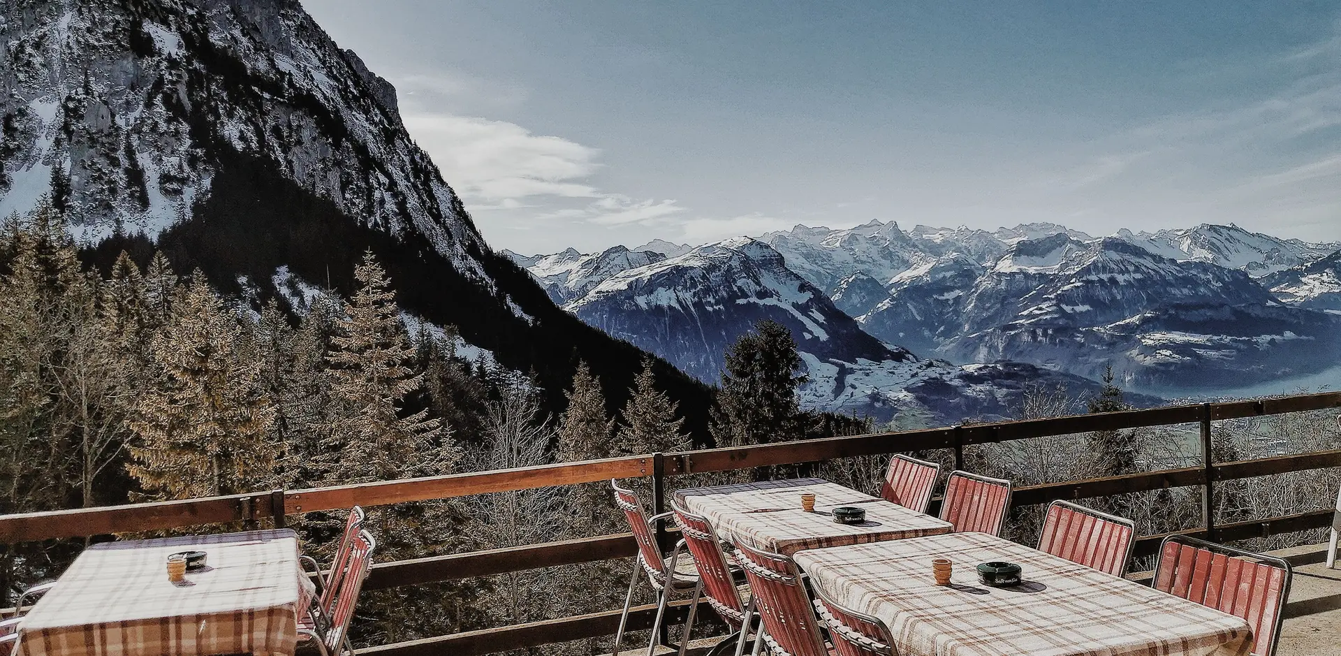 Restaurant tables with checked cloths on a balcony, a jagged snowy peak and a range beyond