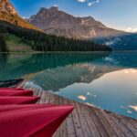 Red canoes stacked on a wooden jetty over a still turquoise lake, a mountain reflected at sunset