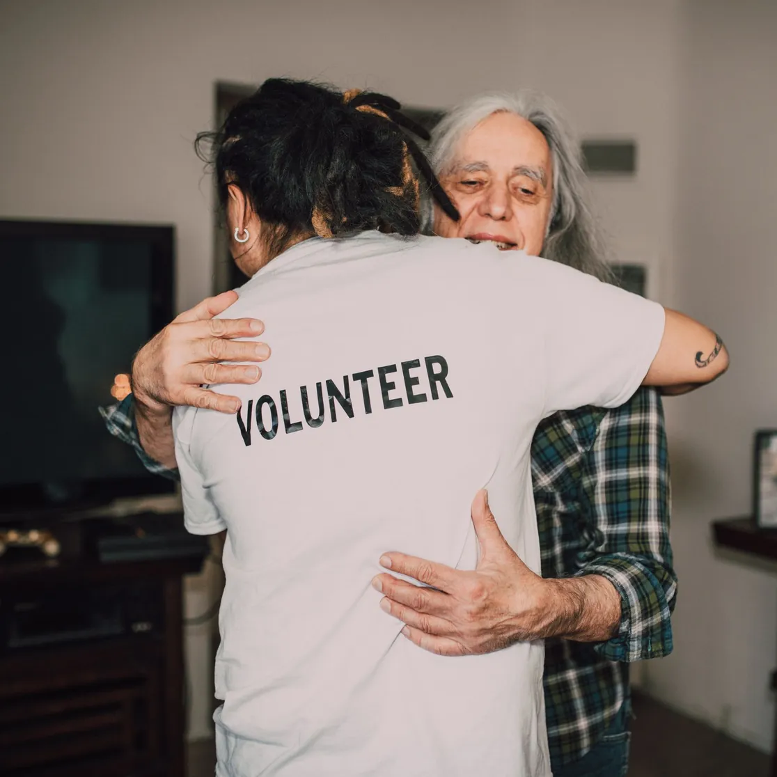 A volunteer hugging an older woman in her living room