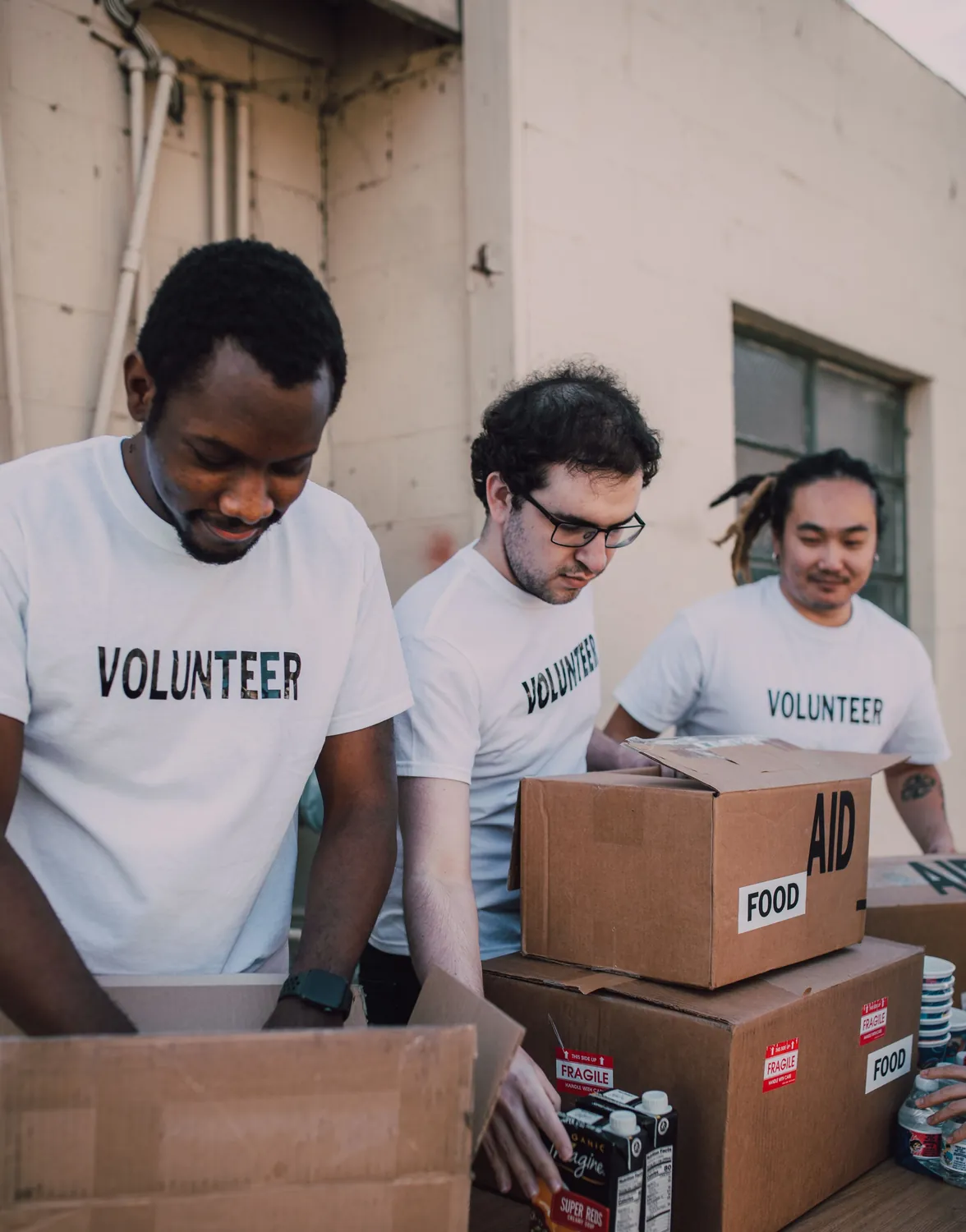 Three volunteers in white VOLUNTEER T-shirts packing cartons of food into boxes marked Aid and Food