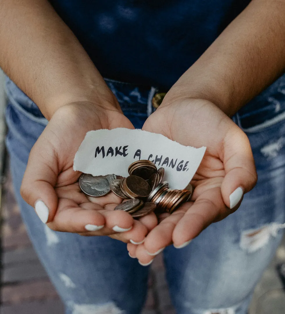 Cupped hands holding a handful of coins and a torn note that reads Make a change