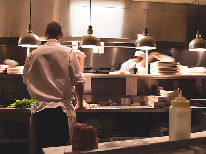 A chef plating a dish at the pass of an open kitchen