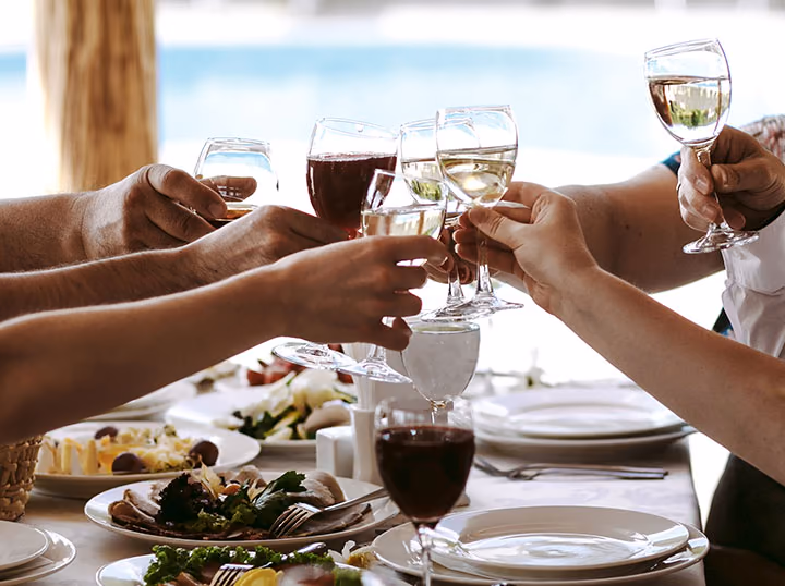 Three people touching whisky glasses together over a laid table