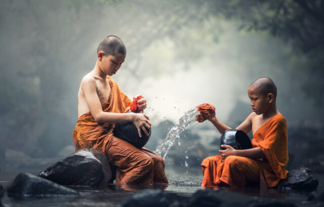 Two young monks in orange robes pouring water during a morning ritual