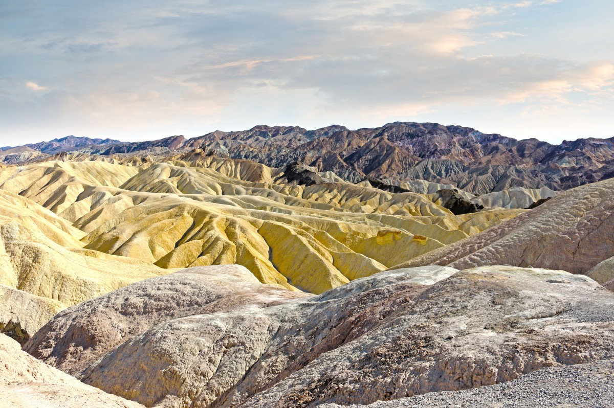 Eroded golden badlands ridges under a pale morning sky, mountains behind