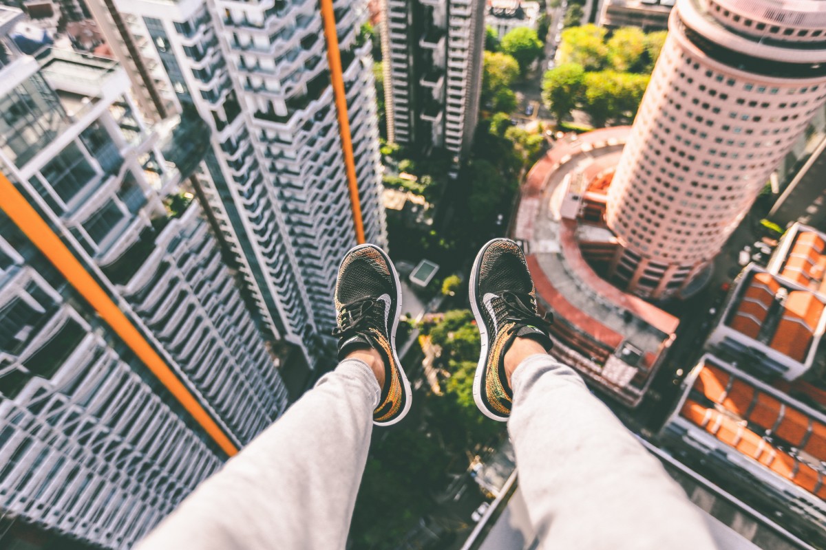 Looking straight down from a rooftop edge at a city far below, the photographer's shoes in frame