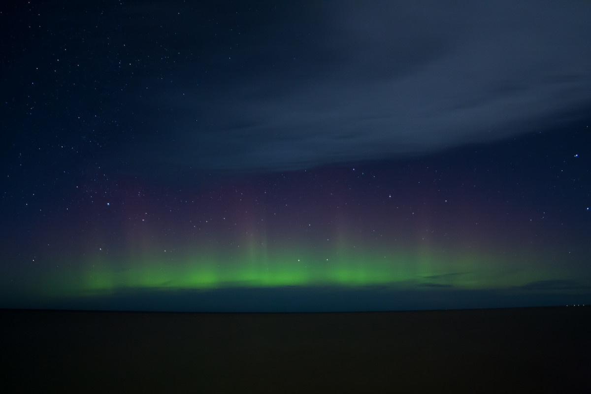 Green aurora borealis low over a dark frozen horizon