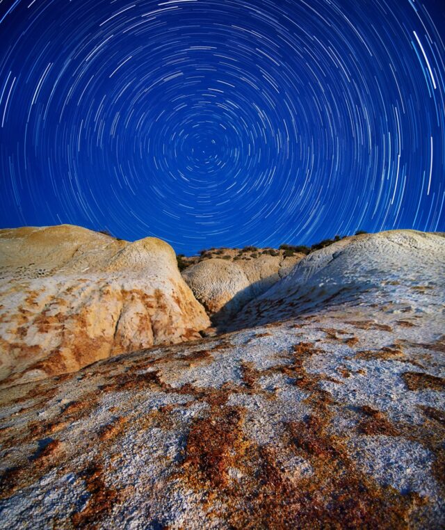 Circular star trails around the celestial pole above a moonlit rock formation