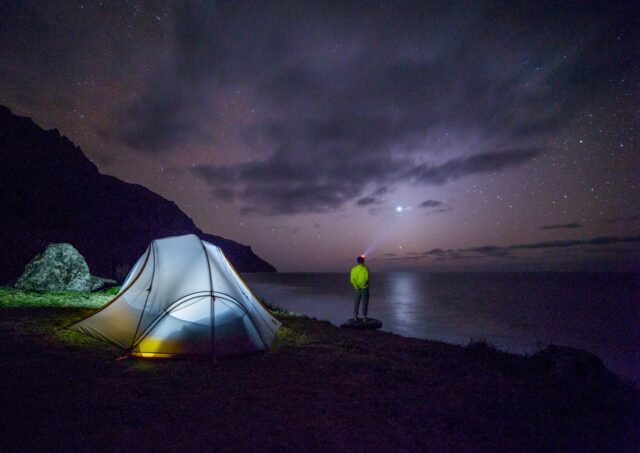 A small illuminated tent beside a lake under a deep blue night sky