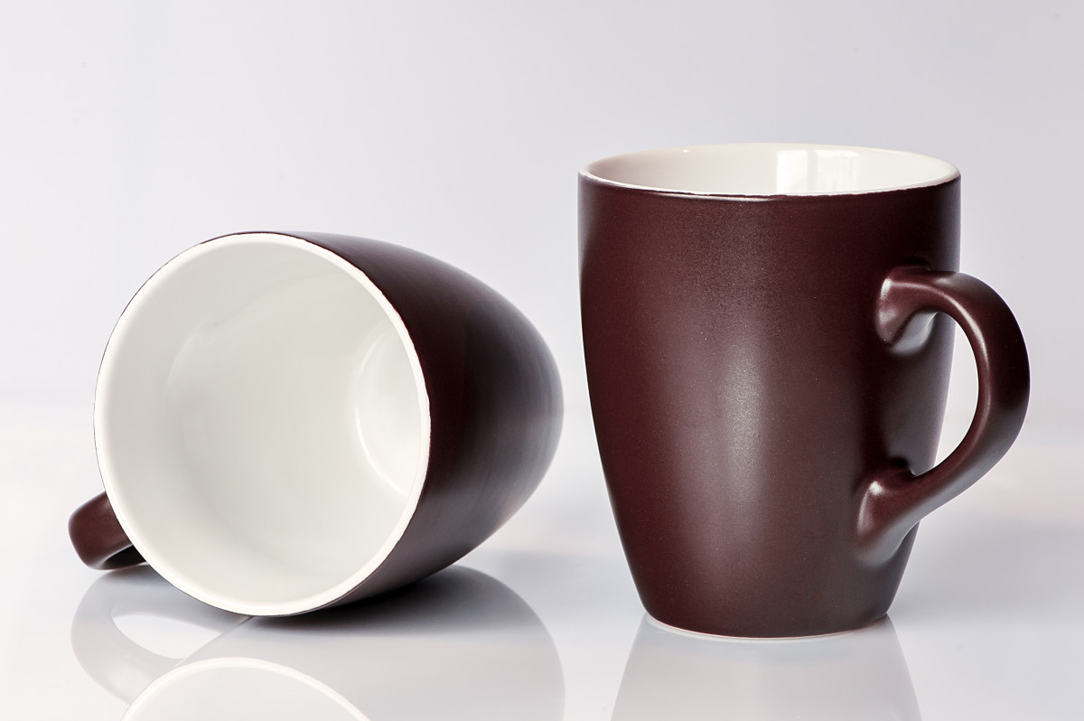 Two ceramic mugs on a white surface, one upright and one on its side