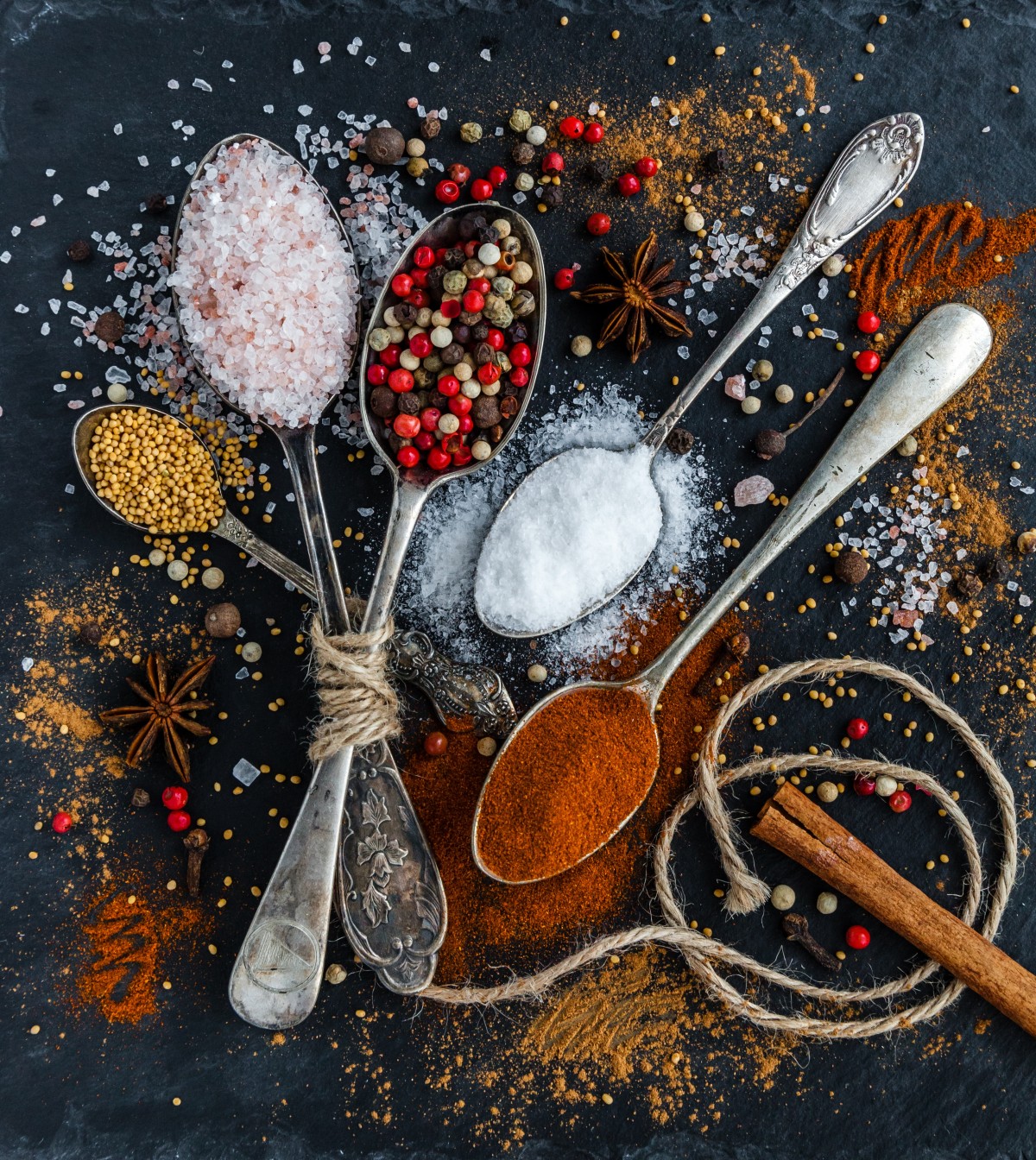 Overhead view of spoons filled with coloured spices arranged on a dark surface