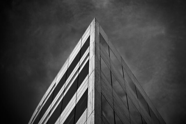 Black and white photograph of an angular modern office building against dramatic clouds