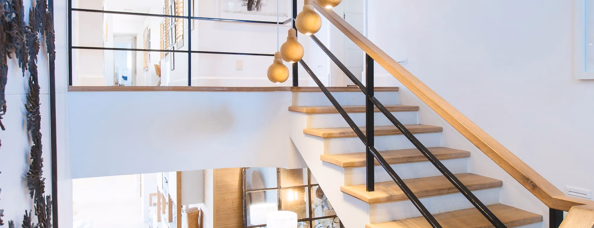 A white stairwell with oak treads, black railings and brass pendant lights