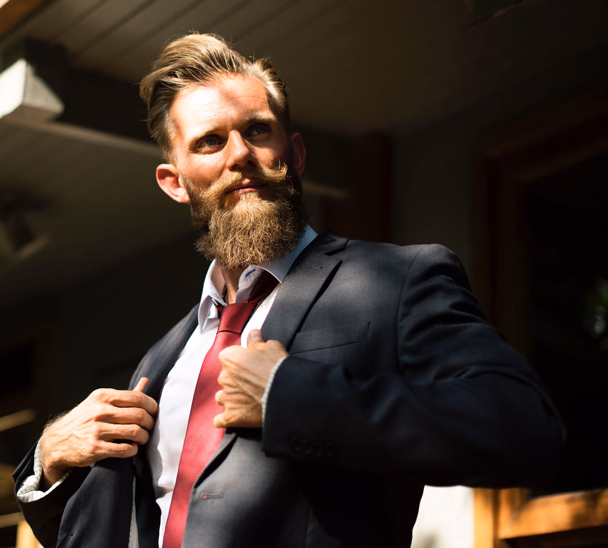 Jeremy Scott, a bearded man in a dark suit and red tie, straightening his jacket