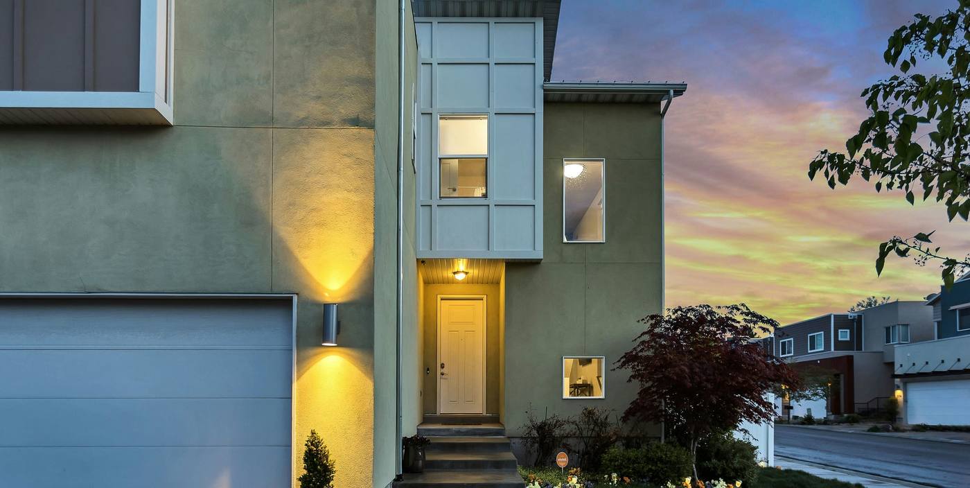 Contemporary townhouse with grey render, a garage door and warm wall lights at dusk